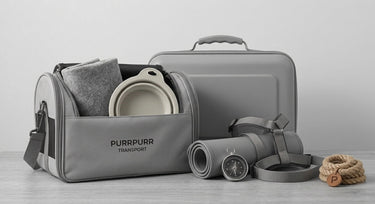 Purrpurr transport and travel accessories for pets in a grayscale flat lay, featuring a grey pet travel bag with branding, a pet carrier case, a rolled travel mat, harness, collapsible bowl, blanket, and a pet rope toy on a light wood background.